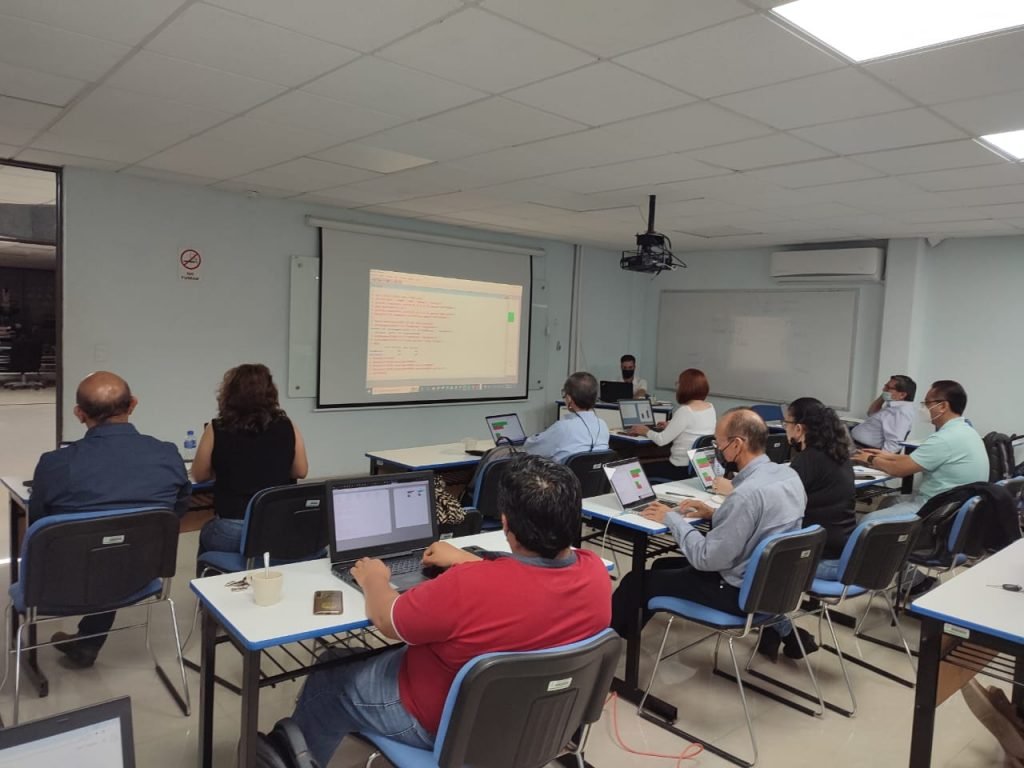 a group of people sitting at tables in a room with laptops